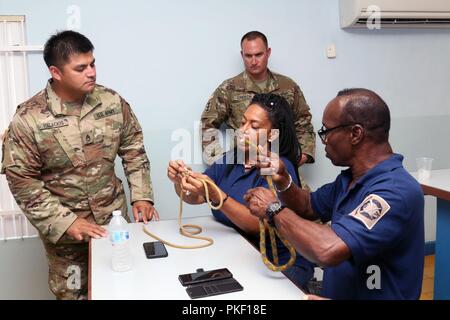 Staff Sgt. José Palacios und Sgt. 1. Klasse Robby E. Creech, mit der Florida National Guard CERFP, unterstützen die Mitglieder des Freikorps Curaçao (VKC) mit Binden ein Doppelzimmer über Hand Knoten bei einer gemeinsamen Informationsaustausch über Camp Suffisant Militärbasis Willemstad, Curaçao. Mitglieder der VKC sind die Vorbereitung für die praktische Entwicklung in der Seil retten und abstoßende, 31. Juli 2018. Stockfoto