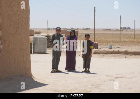 Eine Familie sucht auf der alliierten Soldaten und syrischen Demokratischen Kräfte Verhalten einer Patrouille in der Nähe von Dashisha, Syrien, 31. Juli 2018. Die Koalition unterstützt die syrische Demokratischen Kräfte, um die Sicherheit und Stabilität stärken, Dashisha nach den jüngsten Befreiung der Region von ISIS. Stockfoto