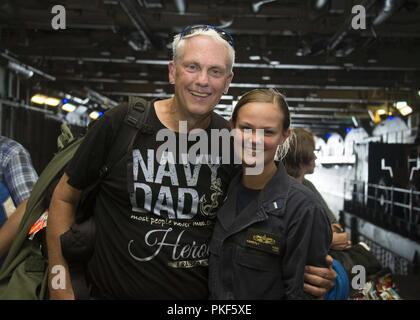 Atlantik (7. August 2018) Lt. j.g. Kimberly König und ihr Vater, Bob, posieren für ein Foto im unteren Fahrzeug Lagerung an Bord der Wasp-Klasse amphibisches Schiff USS Iwo Jima (LHD7), 7. August 2018. Iwo Jima ist Hosting 269 Freunde und Familie Mitglieder für einen Tiger Cruise während mit seinen Amphibischen bereit Gruppe zur Unterstützung der Maritime Security Operations und Theater Sicherheit Zusammenarbeit in Europa und im Mittleren Osten eingesetzt werden. Stockfoto