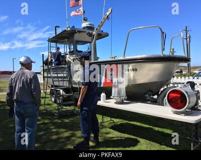 Ein Coast Guard Station Humboldt Bay Mitglied der Besatzung spricht über Coast Guard Vermögenswerte mit einem lokalen Bürger bei der jährlichen Open House Veranstaltung der Station in Samoa, Calif., Aug 11, 2018. Coast Guard Mitglieder sprach mit den Teilnehmern über viele Aufgaben der Küstenwache im Bereich, sofern allgemeine Tipps für die Sicherheit von Boot und zeigte auf, wie die Küstenwache hilft Seemänner aus, die in der Region tätig. Stockfoto