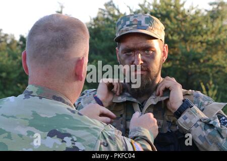 CAMP ÄSCHE, Mich - Pvt. Arturs Arturs Kaupuzs mit Combat Support Unternehmen, 3. Brigade, der Lettischen Nationalen Streitkräften, bereitet sich auf ein Interview als Sgt. Brandon Burk mit 135 Mobile Public Affairs Loslösung, Iowa Army National Guard hilft seinem Lavalier Mikrofon im Camp Äsche, Mich., Nov. 9, 2018 Position. Die USA und der lettischen Armee beteiligen sich an Northern Strike, eine gemeinsame, multinationalen, kombinierte Waffen live Fire Training. Stockfoto