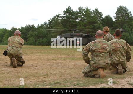 Soldaten der 294. Der Area Support Medical Unternehmen, Iowa Army National Guard, warten Sie, bis das Signal des Flug medic vor der Annäherung an einen UH-60 Blackhawk Hubschrauber während Nördlichen Streik 2018 im Camp Äsche Mich., 7, am 12.08.2018. Die medizinische Evakuierung Ausbildung, bei der Be- und Entladung fiktive Patienten, ist Teil der Teilnahme der Iowa Einheit in der Gemeinsamen multinationalen kombinierte Waffen live Fire Training. Stockfoto