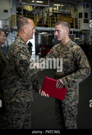 Pazifik - US Marine Sgt. Ilia Karanadze, ein Funker mit dem Maritimen Raid-Kraft, Befehl Element, 13 Marine Expeditionary Unit (MEU), gratuliert von Oberst Krämer Nelms, kommandierender Offizier, 13. MEU, während seiner verdienstvollen Förderung Zeremonie an Bord des Wasp-Klasse amphibisches Schiff USS Essex (LL 2), während einer planmäßigen Einsatz der Essex Amphibious Ready Group (ARG) und die 13. MEU, 8. August 2018. Das Essex ARG/13 MEU Team ist ein ist ein fähiger und tödliche Navy-Marine Corps Team der 7 Bereich der Flotte im Einsatz der regionalen Stabilität zu unterstützen. Stockfoto