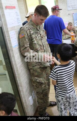 DONGDUCHEON, Republik Korea - Cadet Michael Bertlesman, ein steigender älterer Politische Wissenschaft an der Rochester Institut für Technologie von Plainview, New York, und Cadet Truppe Leadership Training" Teilnehmer in den 6 Battalion, 37th Field Artillery Regiment zugewiesen haben, akzeptiert eine Süßigkeit, die aus einer Student an ein Waisenhaus zum 31. Juli. Bertlesman begleitet sein Sponsor 2. Lt Seth Maddy, eine Brände Zugführer mit 6-37 Th. Soldaten an das Waisenhaus entfernt Ihre Schuhe und Sandalen trug wie in der Republik Korea üblich ist. Stockfoto