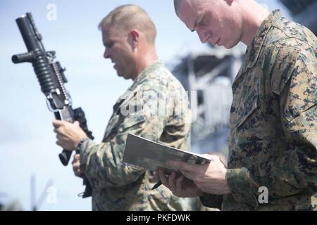 Pazifik - US Marine Oberstleutnant Matthew Danner (links), kommandierender Offizier, Bataillon Landung Team 3/1, 13 Marine Expeditionary Unit (MEU), inspiziert seine Marine M4 Carbine an Bord der Wasp-Klasse amphibisches Schiff USS Essex (LL 2), die während einer planmäßigen Einsatz der Essex Amphibious Ready Group (ARG) und die 13. MEU, 31. Juli 2018. Das Essex ARG/13 MEU Team ist ein fähiger und tödliche Navy-Marine Corps Team der 7 Bereich der Flotte im Einsatz der regionalen Stabilität zu unterstützen, Partner und Verbündeten beruhigen und pflegen eine Präsenz posierten auf eine Krise zu reagieren. Rang Stockfoto