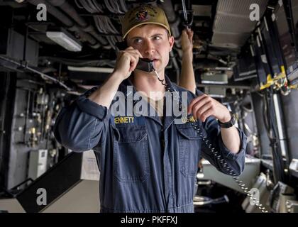 Pazifik (27 Juli 2018) Lieutenant j. g., Nicholas Bennett, von Tampa, Fla., spricht am Telefon beim Stehen Junior Officer der Deck watch in der pilot House San Antonio-Klasse amphibious Transport dock USS Anchorage LPD (23), die während einer planmäßigen Einsatz von Essex Amphibious Ready Group (ARG) und 13th Marine Expeditionary Unit (MEU). Das Essex ARG/MEU Team ist eine starke und flexible Kraft ausgestattet und skalierbar auf jede Krise, die von der humanitären Hilfe und Katastrophenhilfe zu Blindbewerbungen zu reagieren. Stockfoto