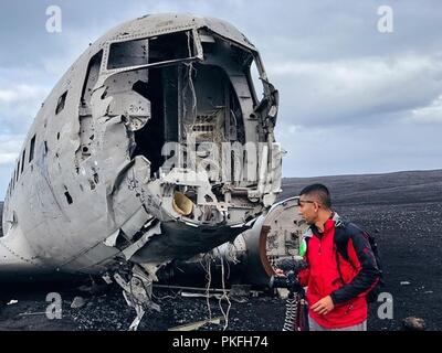 Us Air Force Senior Airman Sukh Bhandari, eine Luft- und Raumfahrt Masse Ausrüstung gesellenprüfung der 509th Maintenance Squadron zugeordnet, beobachtet die US-Marine Super Douglas DC-3 auf den schwarzen Strand von Sólheimasandur, Island am 26. Juni 2018. Das Flugzeug war gezwungen, Land 1973 zum Absturz zu bringen, alle Mitglieder der Besatzung überlebt, aber das Flugzeug verlassen wurde und bleibt am Strand. Stockfoto