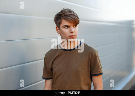 Moderne Porträt eines jungen Mannes mit einer Frisur, die in einem T-Shirt auf grauem Hintergrund Stockfoto