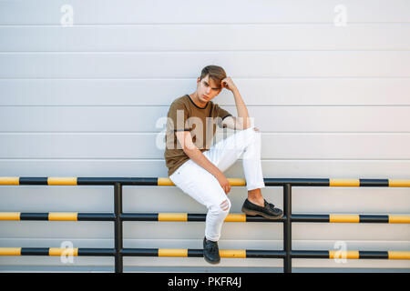 Schönes Modell Mann in modischer Kleidung und Schuhe Leder schwarz liegt in der Nähe einer grauen Wand Stockfoto