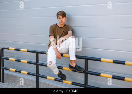 Stilvolle hübscher junger Mann in trendigen Sommer Kleidung in der Nähe der Wand saß Stockfoto