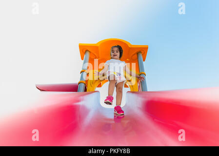 Portrait von niedlichen kleinen Mädchen, das versuchte auf rosa Schieber von Oben nach Unten auf dem Spielplatz zu Fuß Stockfoto