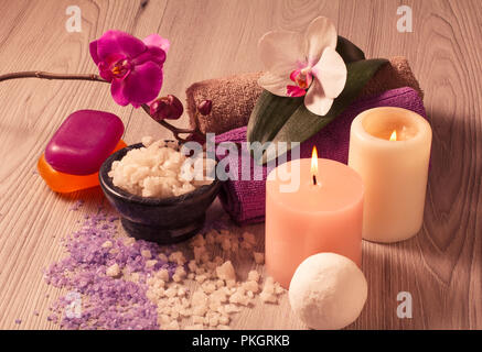 Spa mit Orchideenblüten, Schüssel mit Meersalz, Kerzen, Seife und Handtücher auf Holzbrett Stockfoto