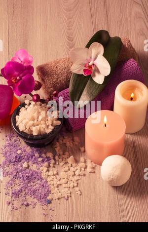 Spa mit Orchideenblüten, Schüssel mit Meersalz, Kerzen, Seife und Handtücher auf Holzbrett Stockfoto