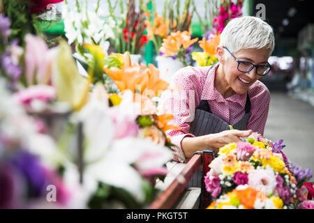 Charrming senior Frau arrangiert Blumen auf dem lokalen Markt Stockfoto