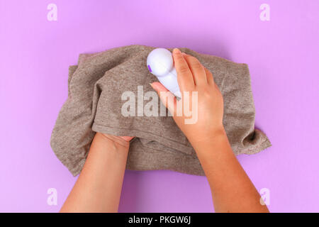 Eine Maschine zum Entfernen von Flusen in der Hand. Pullover mit Bommel auf lila Pastell Hintergrund Stockfoto