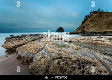 Sonnenaufgang am Cape Kiwanda, Oregon mit den Felsen im Vordergrund und Haystack Rock im Hintergrund Stockfoto