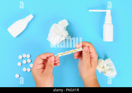 Ein Mann hält ein Thermometer in seine Hand mit einer hohen Temperatur vor einem blauen Tisch mit Tabletten. Top Anzeigen, Kopieren, flach Stockfoto