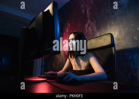 Portraitfotos mit einem lächelnden Schönen professionelle Gamer Mädchen spielen in First Person Shooter Online Video Spiel auf Ihrem eigenen Computer. Lässig süß Geek sprechen in Headset Stockfoto