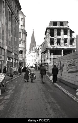 1950er Jahre, historische, Koln, Deutschland, Menschen zu Fuß entlang einer Straße im Stadtzentrum, neben einer Bombe Website und zerstörte Gebäude von WW 2. Die Kathedrale der Stadt, die nicht trotz der Bombardierungen zerstört wurde, im Hintergrund gesehen werden kann. Stockfoto