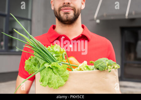 Teilansicht der Mann in der roten Uniform holding Papiertüte mit frischem Gemüse Stockfoto