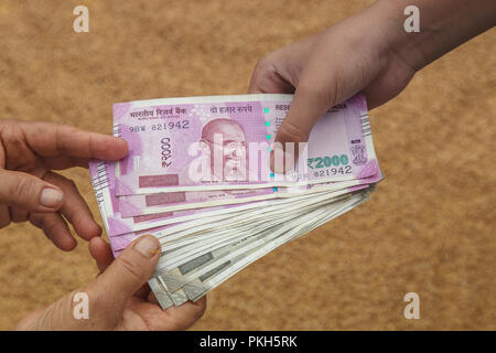 Hand geben Indische 500 und 2000 Rupien Banknoten über Weizen Hintergrund. Konzept für das Ergebnis oder verbringen Sie in der Landwirtschaft. Stockfoto