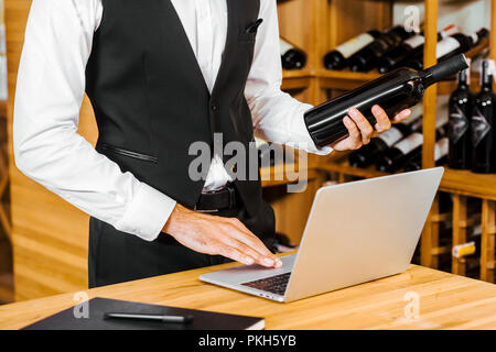 7/8 Schuß Wein Steward holding Flasche und Arbeiten mit Laptop bei Wein, Stockfoto