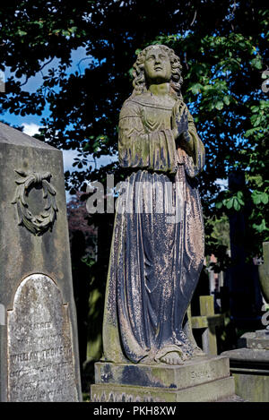 Viktorianische Statue einer Frau mit ihre Hände im Gebet vor dem Hintergrund der Bäume auf dem Friedhof von Dean, Edinburgh. Stockfoto