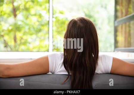 Rückansicht eines Frau sitzt auf einem Sofa vor dem Fenster Stockfoto