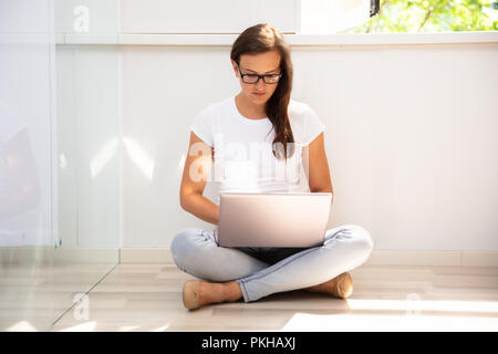Junge Frau sitzt auf dem Boden mit Laptop Stockfoto