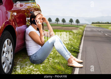 Seitenansicht von depressiven Frau sitzt auf der Straße in der Nähe von Panne Auto Stockfoto