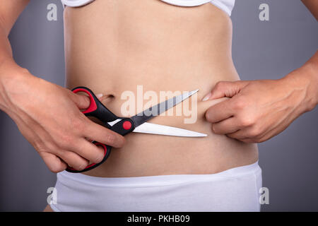 Mittelteil Der eine Frau Hand Bauch Fett mit einer Schere Stockfoto