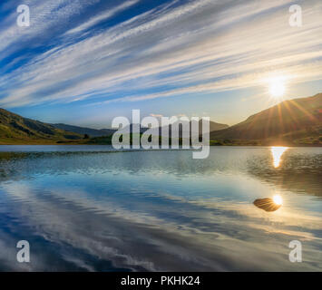 Der See Llynnau Mymbyr wider den blauen Himmel, Wolken und Sonne mit Mount Snowdon im Hintergrund. Snowdonia (Eryri), Wales (Cymru), UK. Stockfoto