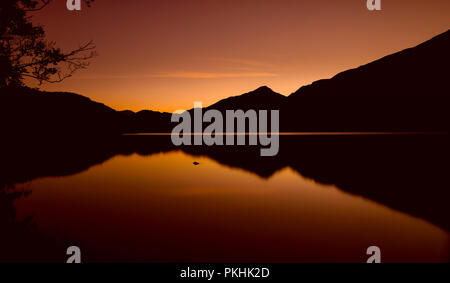 Die Sonne ist hinter den Bergen um Llyn Gwynant, ein See in Snowdonia (Eryri), Wales (Cymru), UK. Ein verbrannter Himmel silhouetting die Berge, Cast Stockfoto