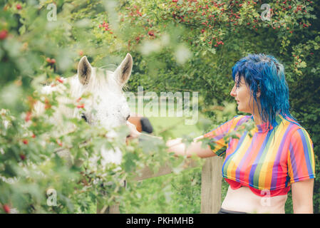 Eine blaue behaarte Frau Anschläge ein weißes Pferd auf einer Weide Stockfoto