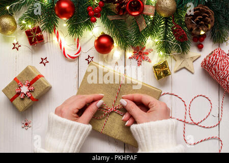 Der Frau die Hände binden bis Weihnachten Geschenk Box auf weiße Holztisch mit festlichen Dekorationen und Lichter Stockfoto