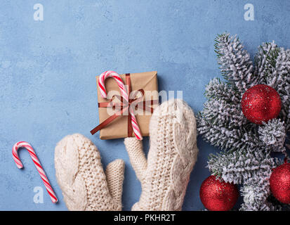 Hände in Handschuhe mit Geschenk Box. Festliche winter Hintergrund auf Blau Stockfoto