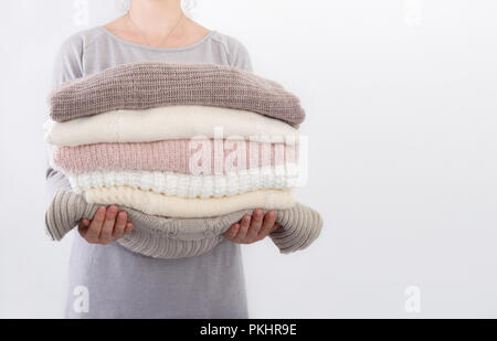 Stapel von gemütlichen gestrickte Pullover oder Decken Pastell Trend Farben in die Hände einer jungen Frau gegen die Wand Stockfoto