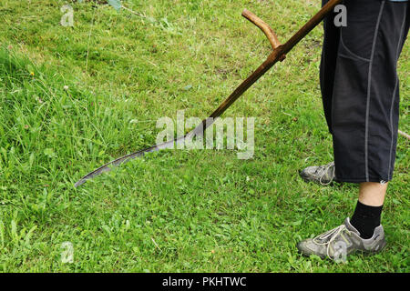 Ein Mann ein Gras mähen mit der Sense. Dieses Werkzeug ist aus Holz und Stahl Kante zusammenbauen. Sommer job Stockfoto