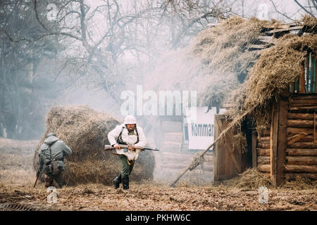 Rogachev, Belarus - Februar 25, 2017: Re-Enactor gekleidet als Soldat in der deutschen Wehrmacht Infanterie WW II läuft auf dem Schlachtfeld in der Nähe von brennenden Holz- Hou Stockfoto