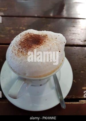 Nahaufnahme auf einem schlichten weißen Tasse Kaffee mit Milchschaum nach latte Stil auf braunem Holz- Tisch in einem Café. Stockfoto