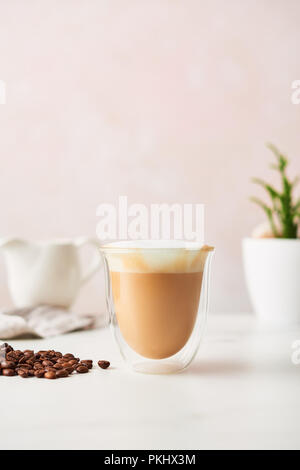 Cappuccino in einem doppelwandigen Glas mit gerösteten Kaffeebohnen. Feminine rose Hintergrund mit kopieren. Bild mit hoher Auflösung. Stockfoto