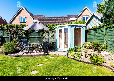 Englischer Garten, Gartenhaus, Terrasse, Tisch und Stühle draußen, umzäunter Garten, Trittsteine, Regenschirm über Tabelle, Sommerhäuser, UK, England, Stockfoto