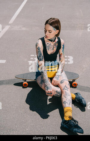 Stilvolle junge Frau mit Tattoos auf Skateboard am Parkplatz Stockfoto