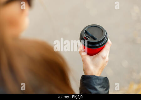 Junges Mädchen hält einen köstlichen Kaffee in einem roten Tasse und geht auf die Straße Stockfoto