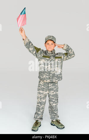 Little Boy in der Tarnung Bekleidung salutierte Halten amerikanische Fahnenmast Hand isoliert auf Grau Stockfoto