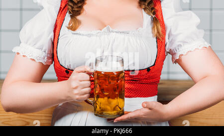 Zugeschnittenes Bild der oktoberfest Kellnerin in traditionellen deutschen Kleid holding Tasse helles Bier in der Nähe von bar Counter Stockfoto