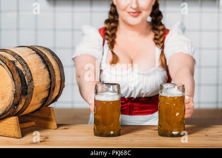 Oktoberfest Kellnerin im traditionellen bayerischen Dress putting Glaskrüge helles Bier am Tresen mit Barrel Bier Stockfoto