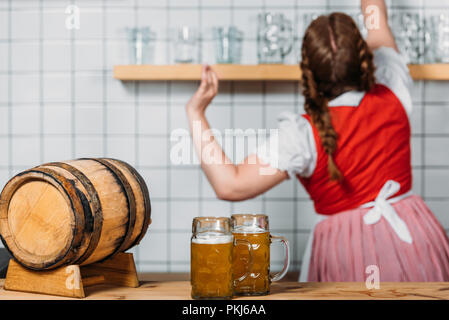 Selektiver Fokus der Zylinder und zwei Becher helles Bier am Tresen und Kellnerin hinter arbeiten Stockfoto