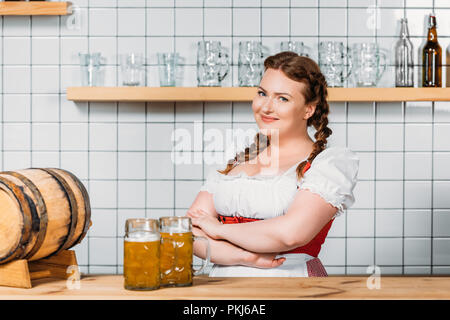 Happy oktoberfest Kellnerin im traditionellen bayerischen Kleid stehen an der Theke mit Tassen von Licht Bier und Barrel Bier Stockfoto