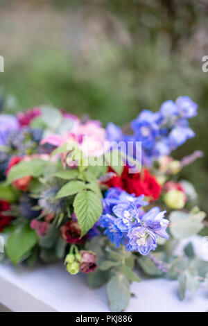 Längliche Blumenschmuck in Vintage metall Vase. Tabelle einstellen. Blaue und rote Farbe. Wunderschönen Blumenstrauß aus verschiedenen Blumen. Park auf Hintergrund Stockfoto